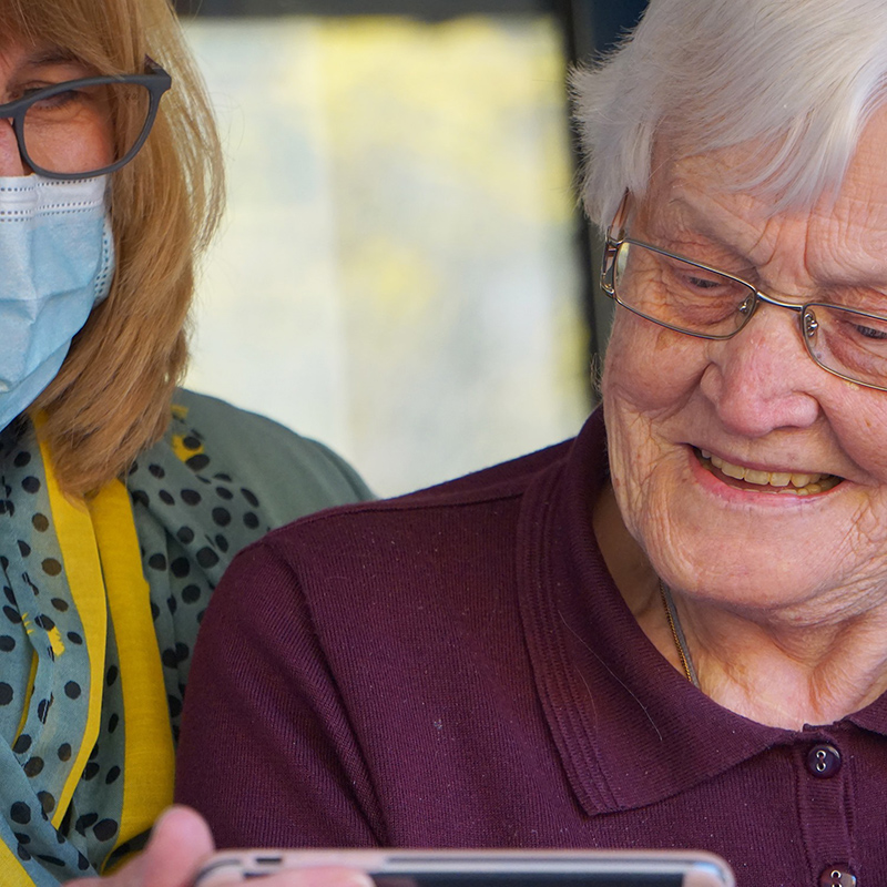 woman in hospital mask assisting senior woman with smartphone